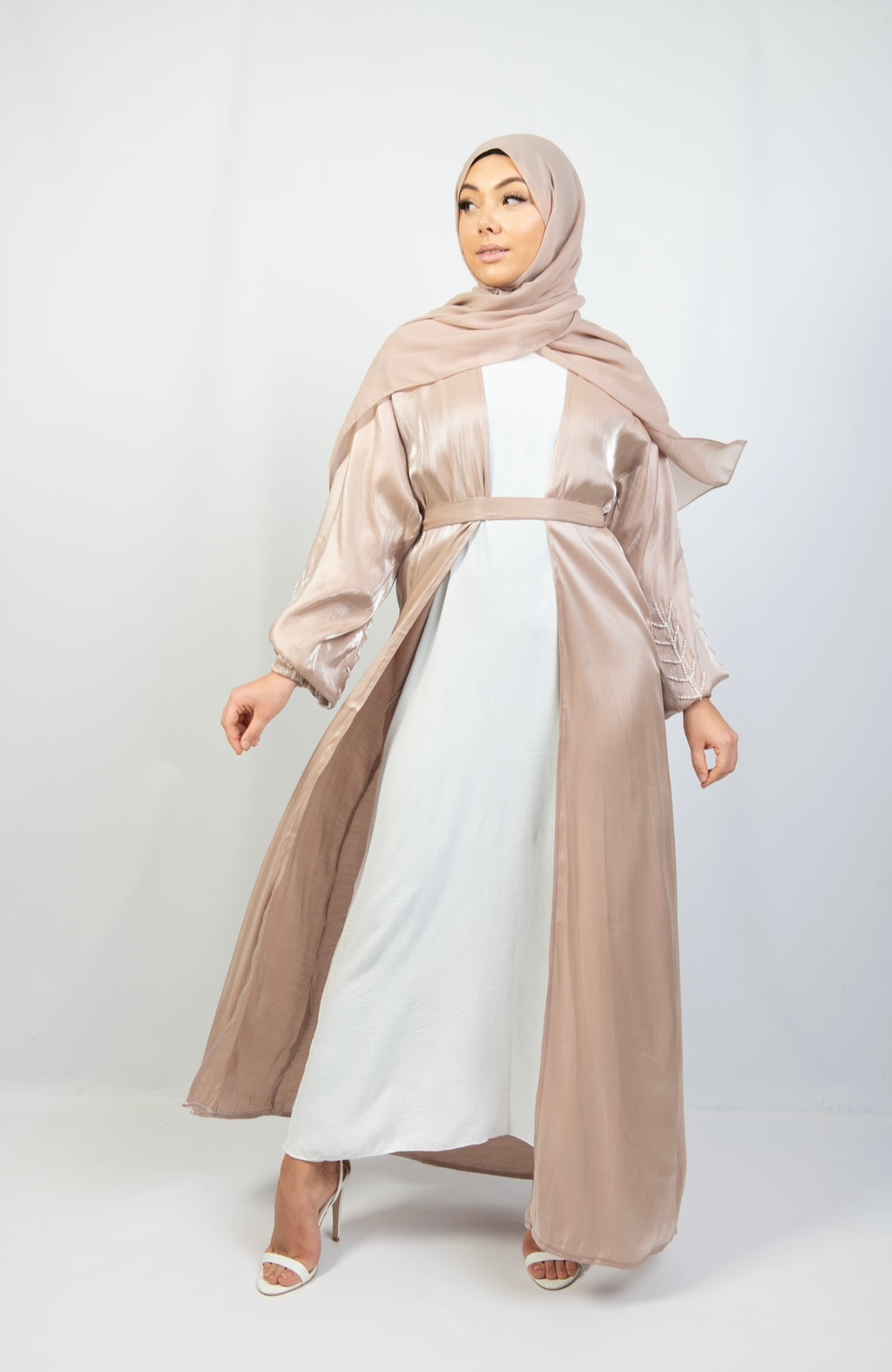 A woman wearing a beige and white kimono set with stone work on the cuffs, paired with a matching headscarf.