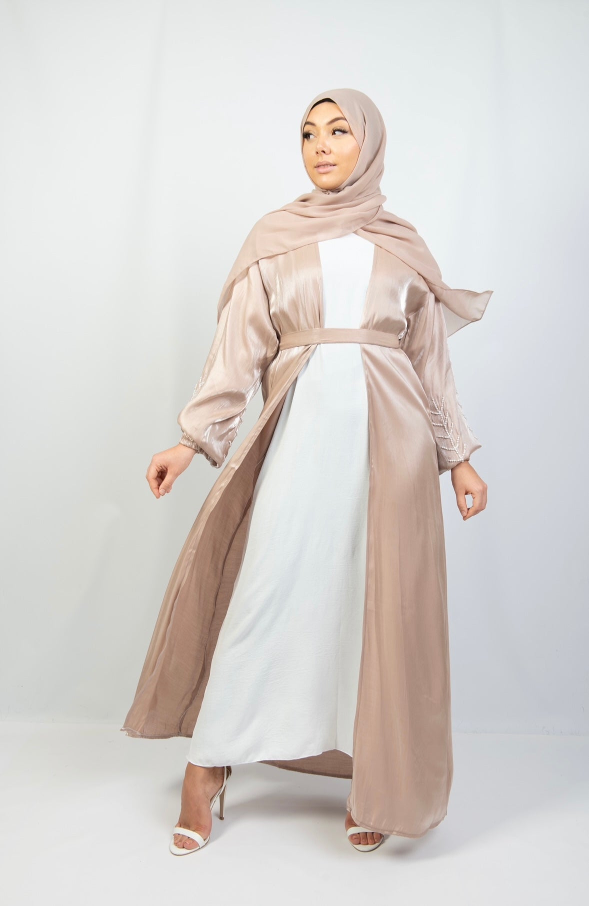 A woman wearing a beige and white kimono set with stone work on the cuffs, paired with a matching headscarf.