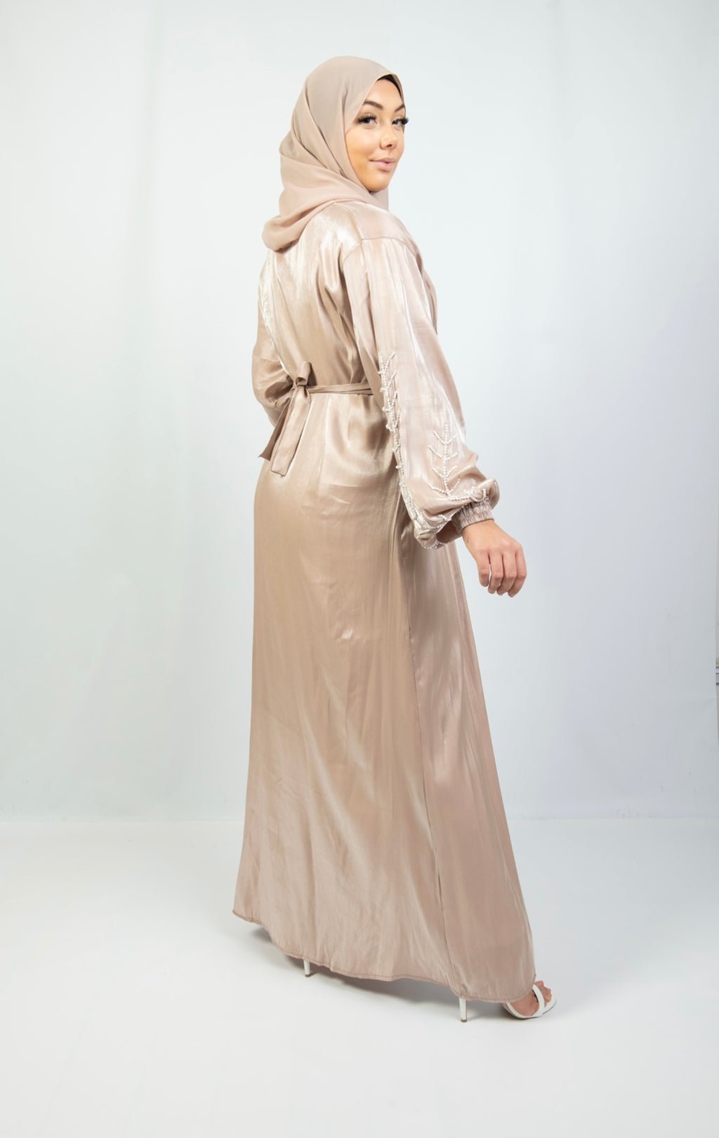 A woman wearing a beige and white kimono set with stone work on the cuffs, paired with a matching headscarf.