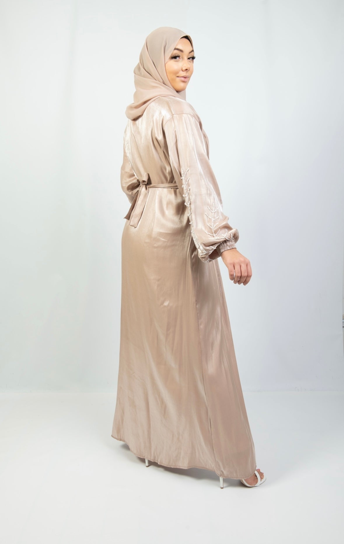 A woman wearing a beige and white kimono set with stone work on the cuffs, paired with a matching headscarf.