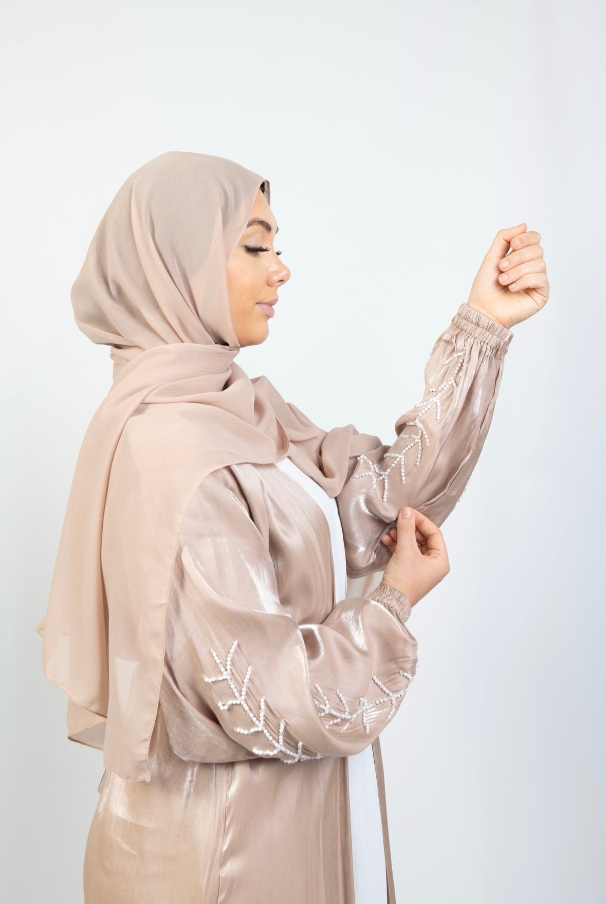 A woman wearing a beige and white kimono set with stone work on the cuffs, paired with a matching headscarf.