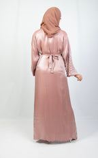 A woman wearing a pink and white kimono set with stone work on the cuffs, paired with a matching headscarf.