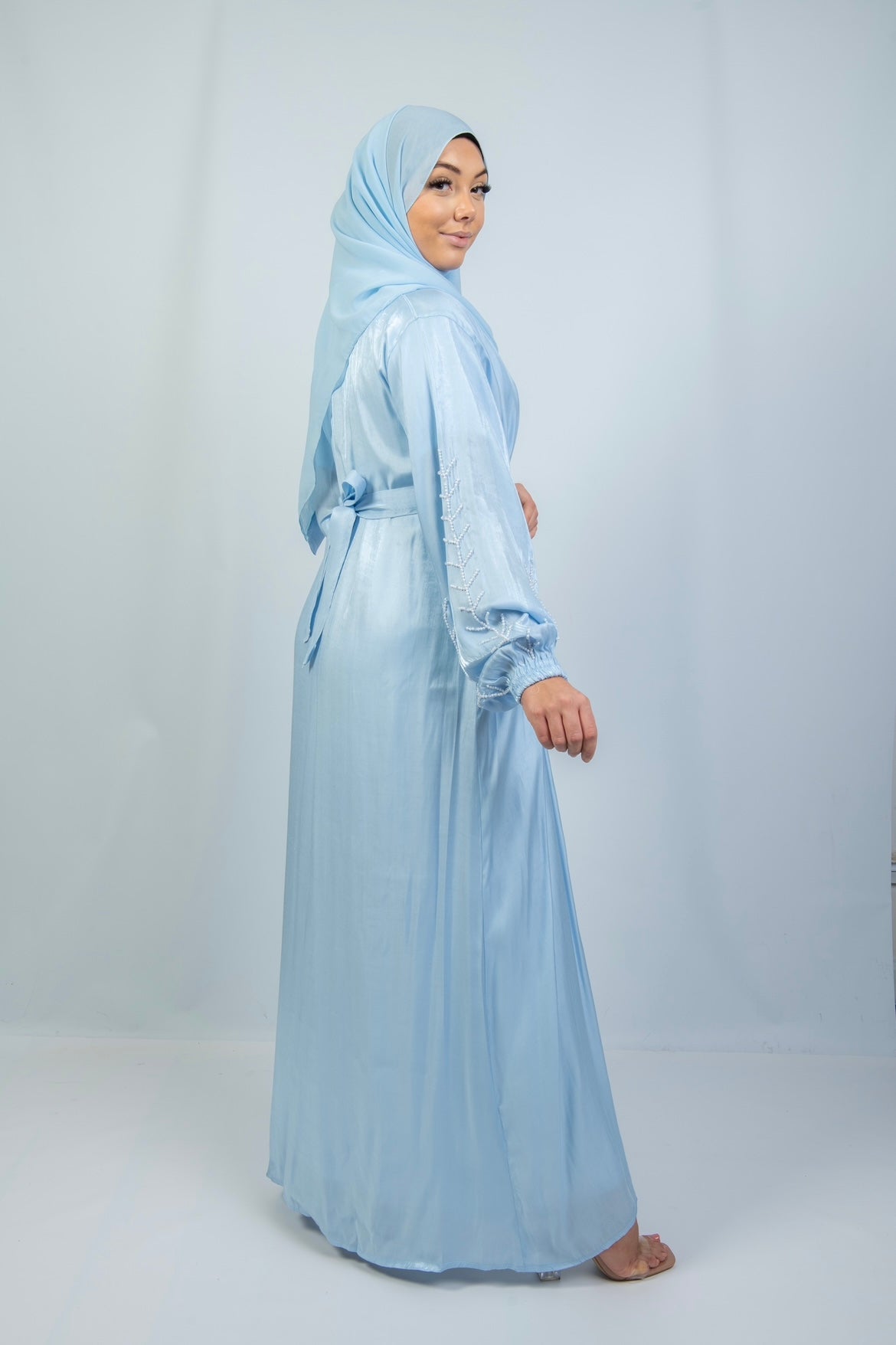 A woman wearing a blue kimono set with white stone work on the cuffs, standing against a plain background.