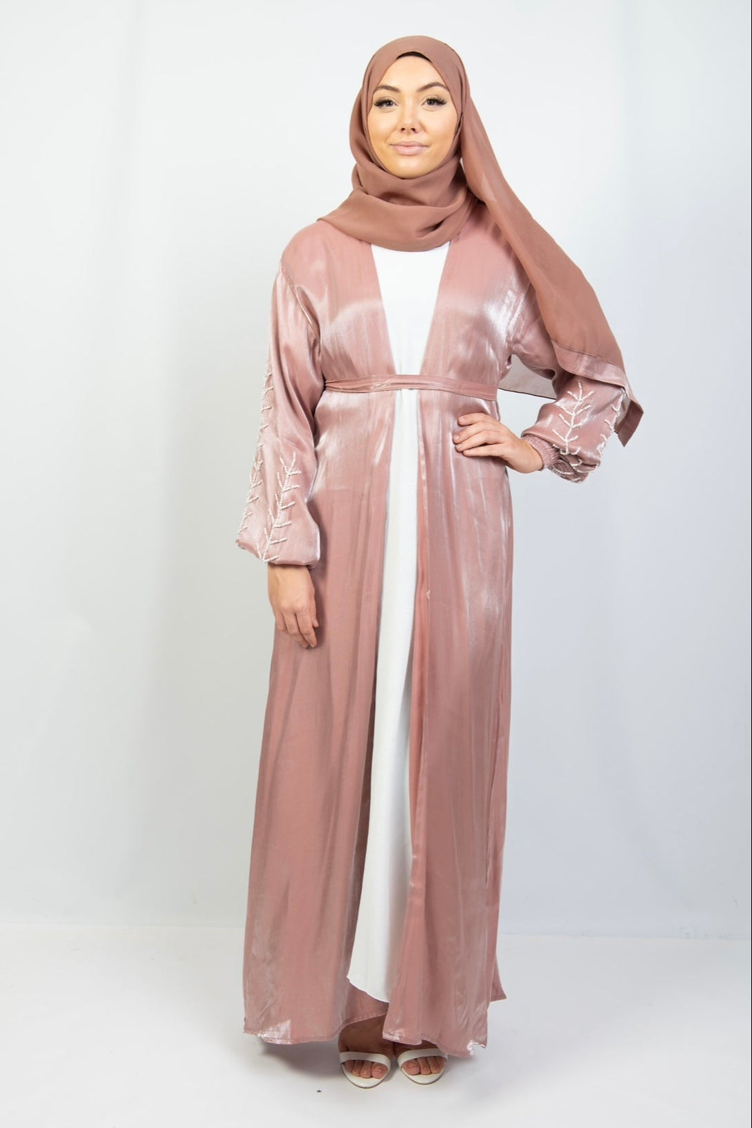 A woman wearing a pink kimono set with white stone work on the cuffs, standing against a plain background.