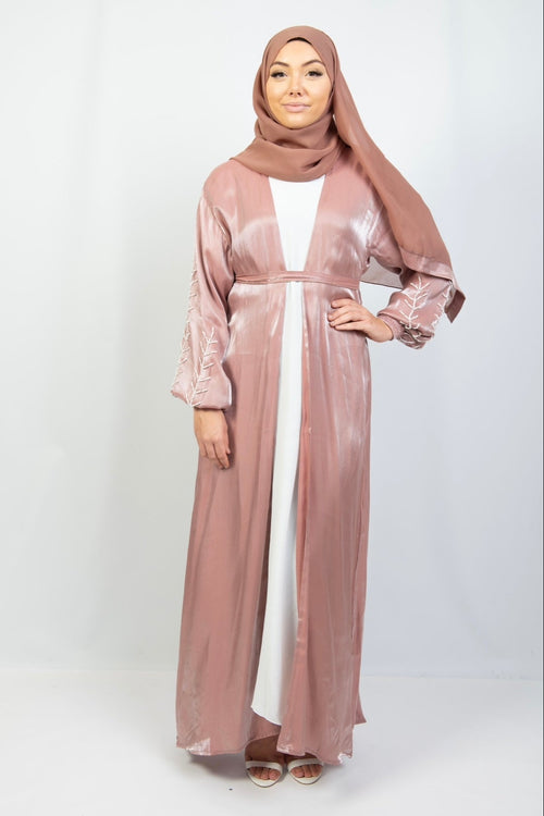 A woman wearing a pink kimono set with white stone work on the cuffs, standing against a plain background.