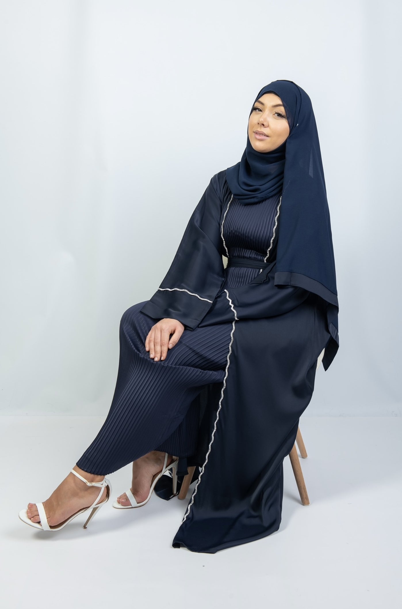A woman seated wearing a full-length kimono in shades of blue with detailed stitching, paired with a matching blue headscarf.