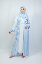 A woman wearing a blue kimono set with white stone work on the cuffs, standing against a plain background.